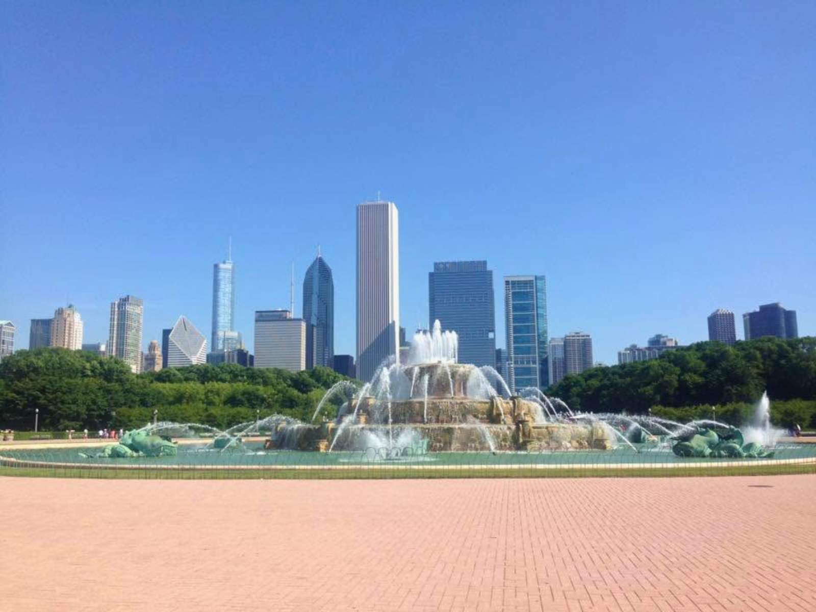 Buckingham Fountain in full flow against the Chicago skyline on a brilliant summer day, the city's towers rising sharp and clear above Grant Park.