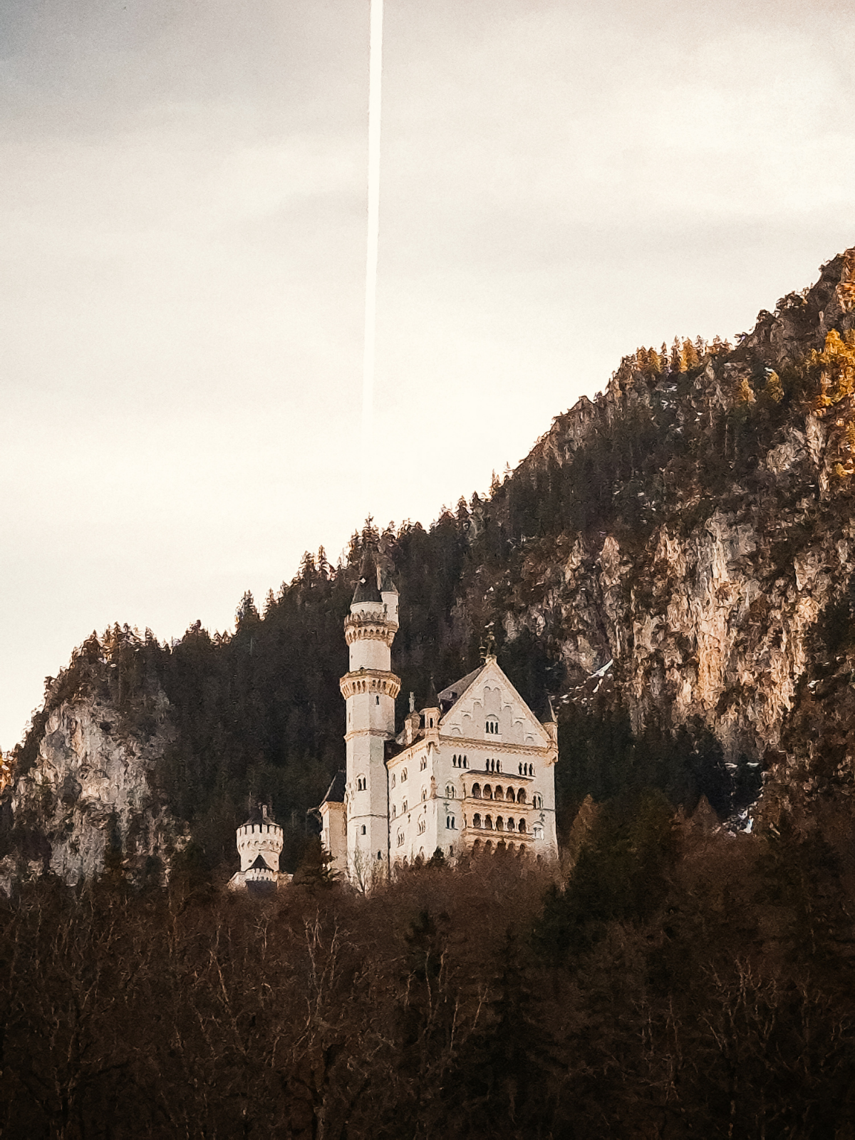 Neuschwanstein Castle perched on a forested cliff in winter light, a single contrail streaking the pale sky above its white towers.