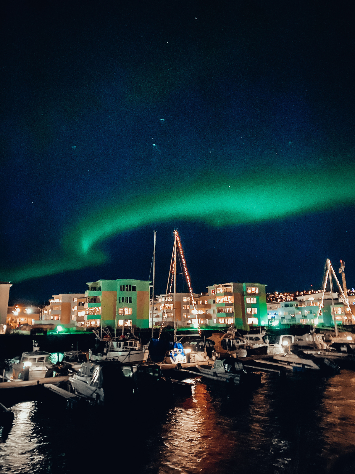 The aurora borealis sweeps in vivid green across the night sky above Tromsø's harbour.
