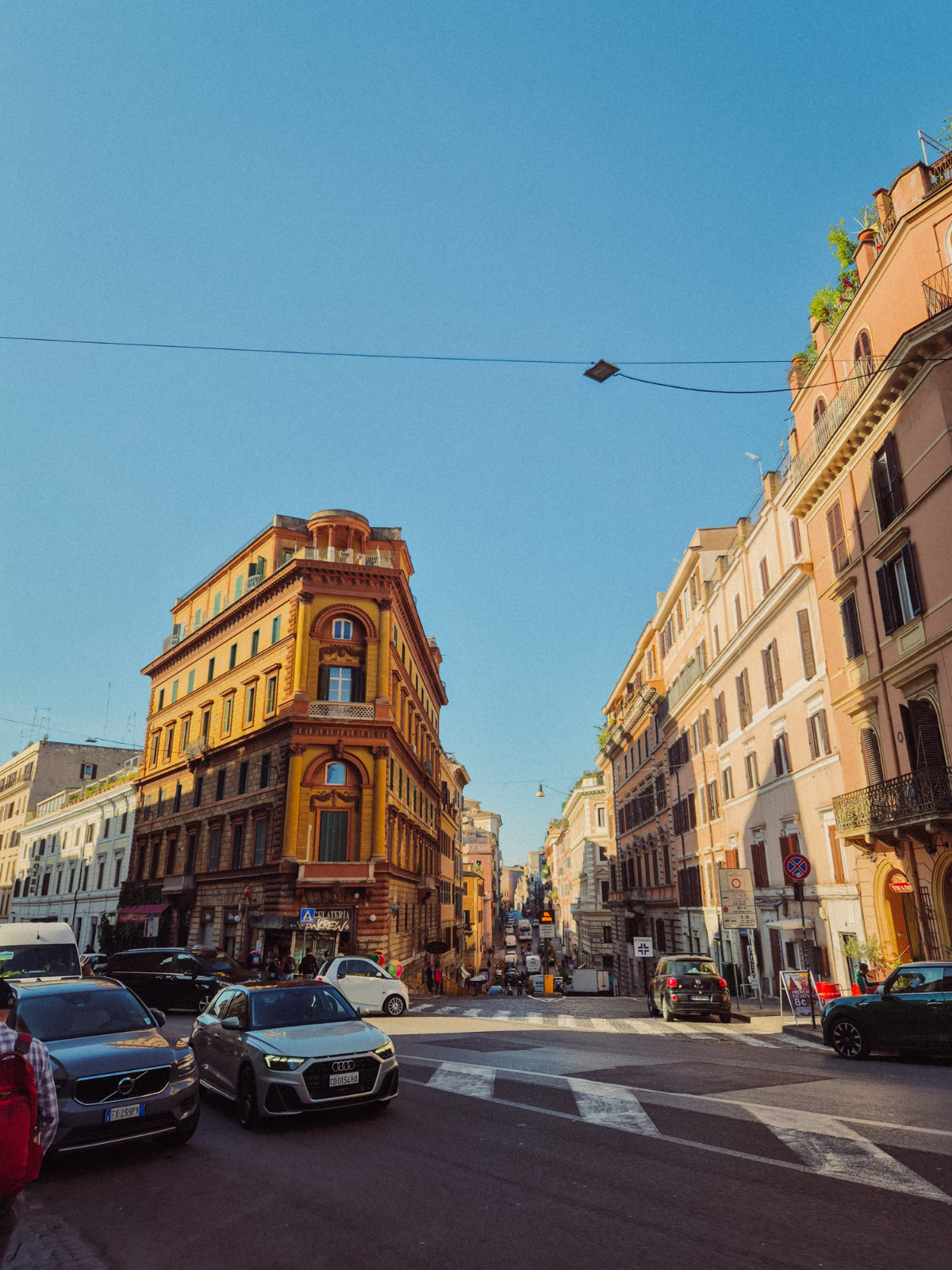 A golden afternoon street corner in Rome, a mustard-yellow flatiron building catching the sun at the junction of two busy roads.