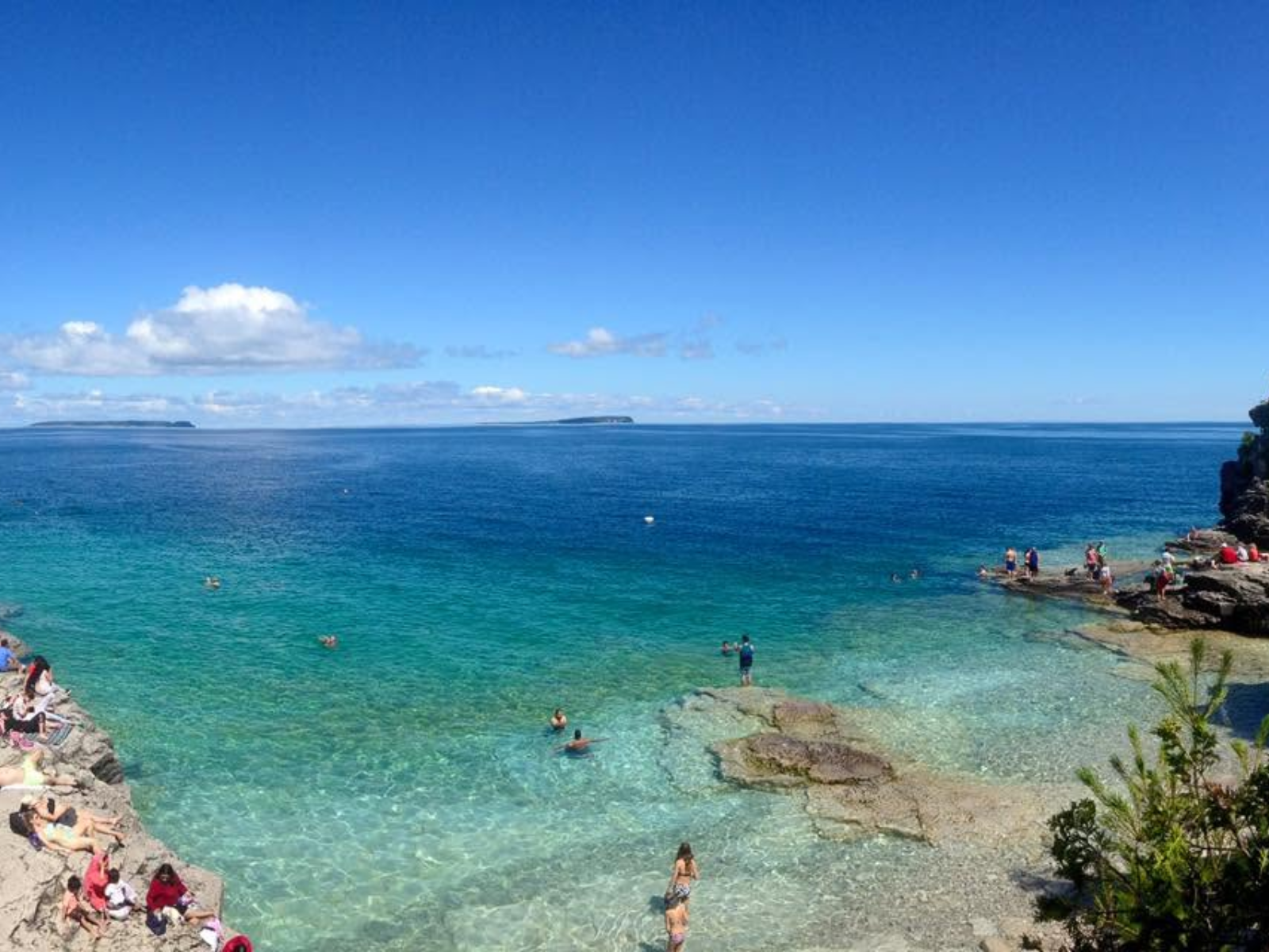 The impossibly clear turquoise waters of The Grotto on Ontario's Bruce Peninsula, people swimming and sunbathing on the rocky Georgian Bay shoreline.