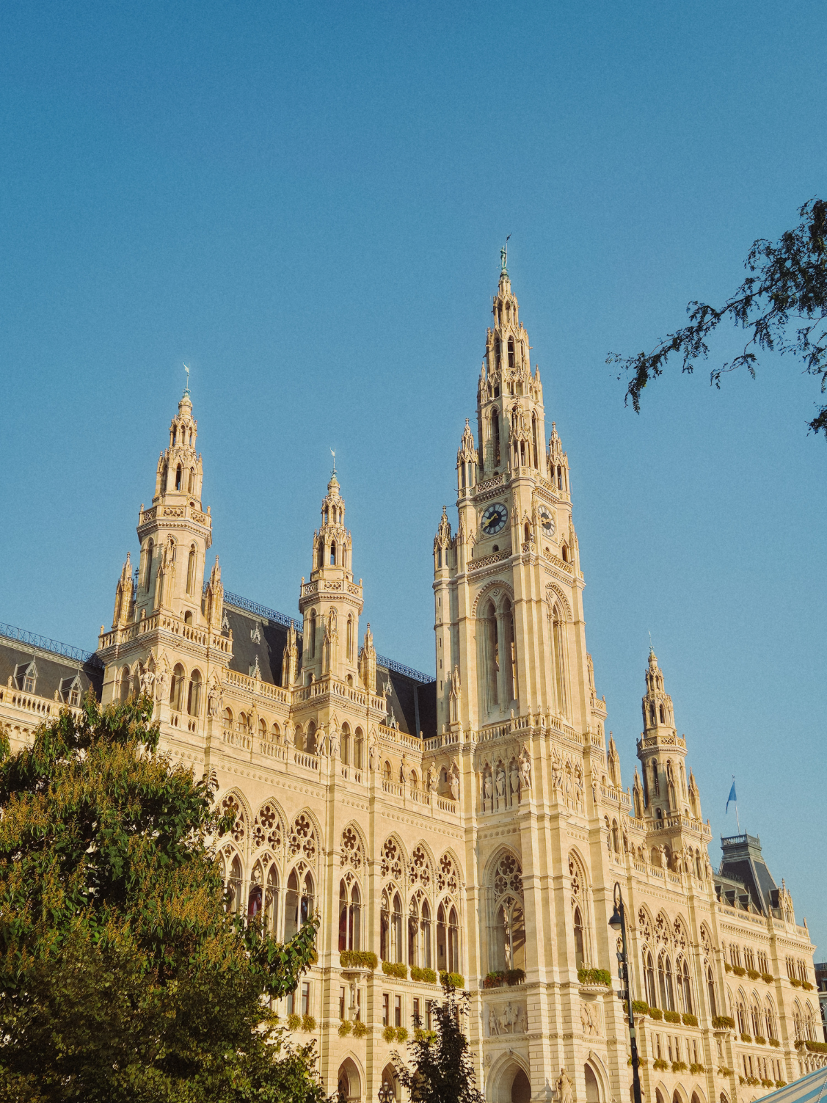 Vienna's neo-Gothic City Hall rising into a cloudless blue sky, its ornate stone towers and spires glowing gold in the morning sun.
