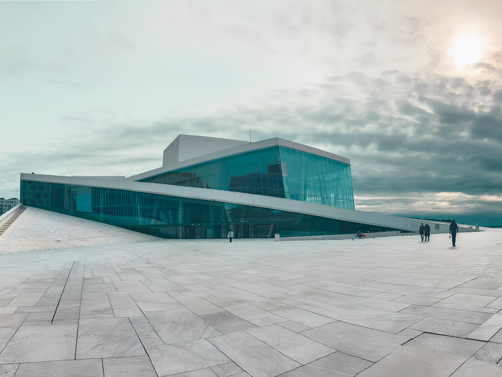 The Oslo Opera House rising from the waterfront on a moody overcast day, its angular white marble roof sloping down to meet the fjord